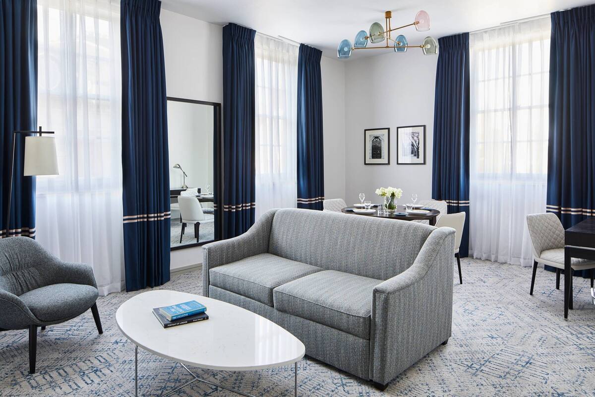 A modern hotel room with a grey sofa, a round white table, and a blue patterned carpet.