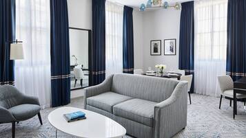 A modern hotel room with a grey sofa, a round white table, and a blue patterned carpet.