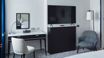 A hotel room with a bed, a desk with a chair, a television, a mirror, and a lamp.