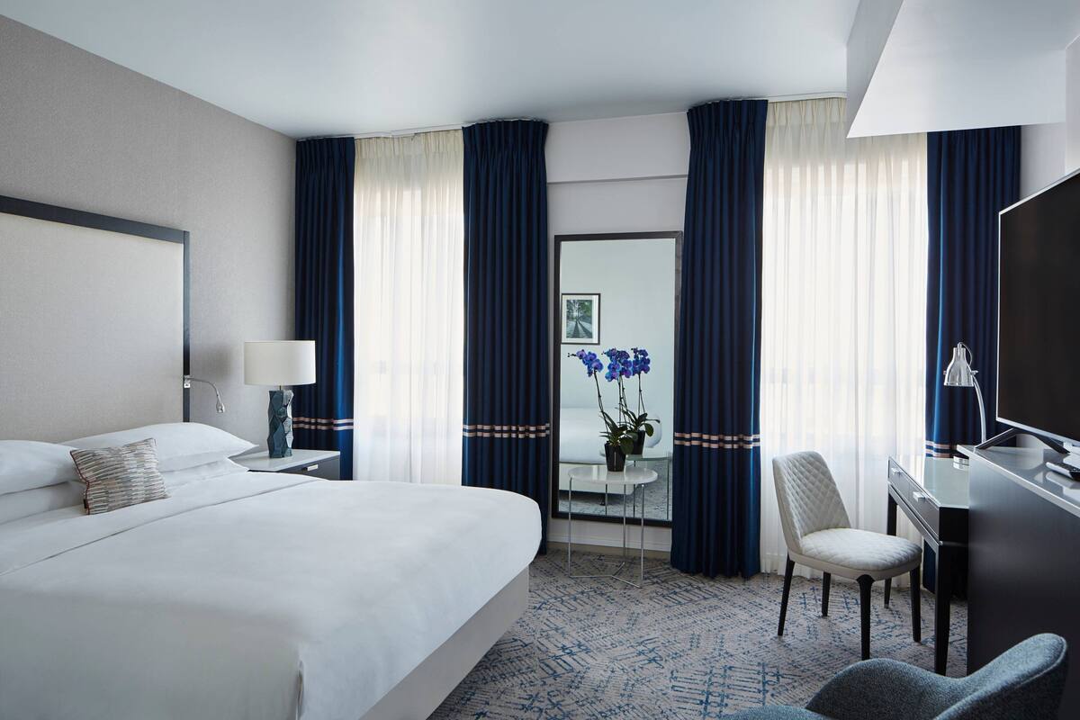 A hotel room with a large bed, a desk, a chair, and a TV.
