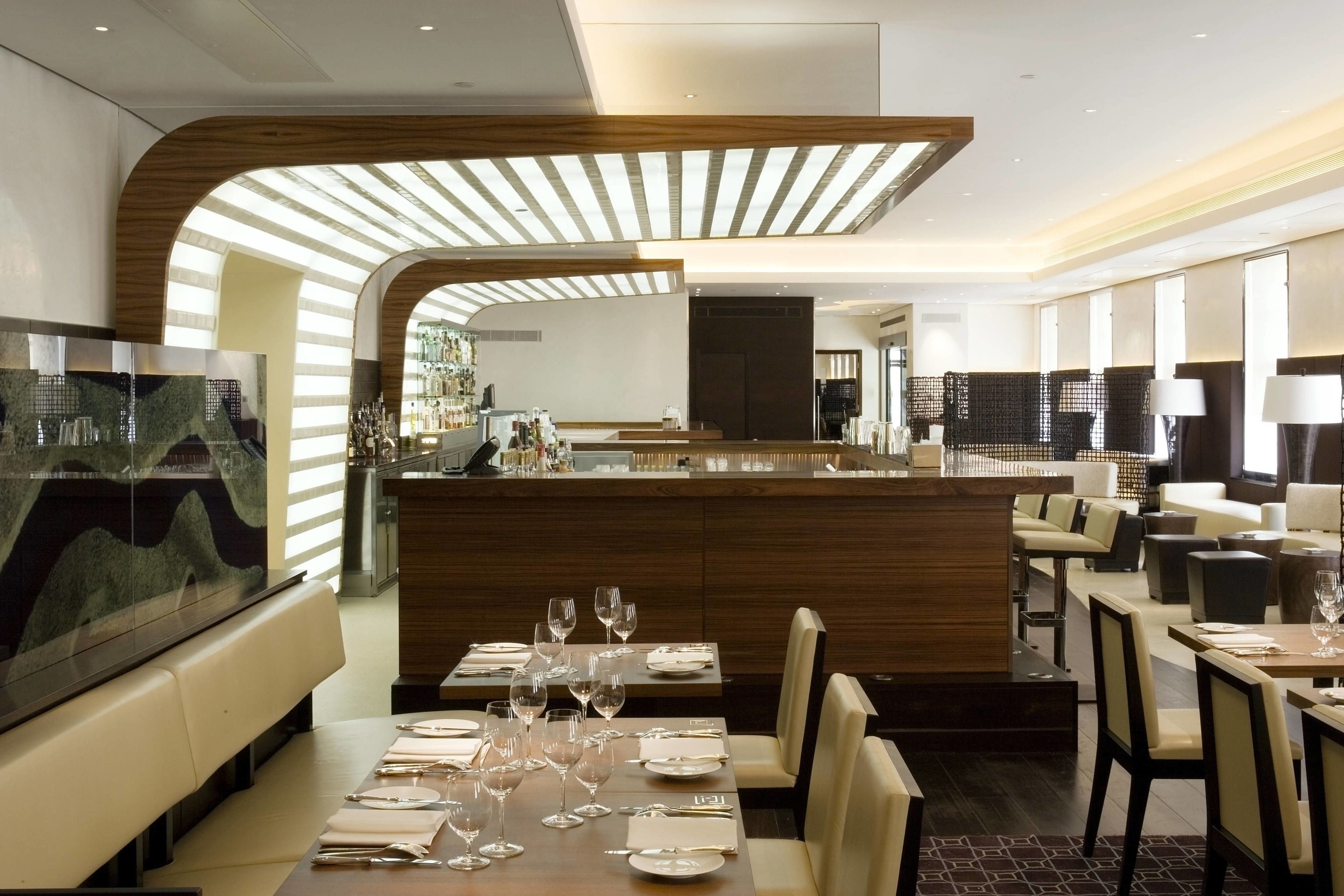 A modern restaurant with a central bar, dining tables with chairs, and a large TV screen.