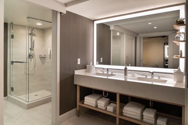 Un baño moderno con ducha de vidrio, un espejo grande y tocador con encimera de mármol.