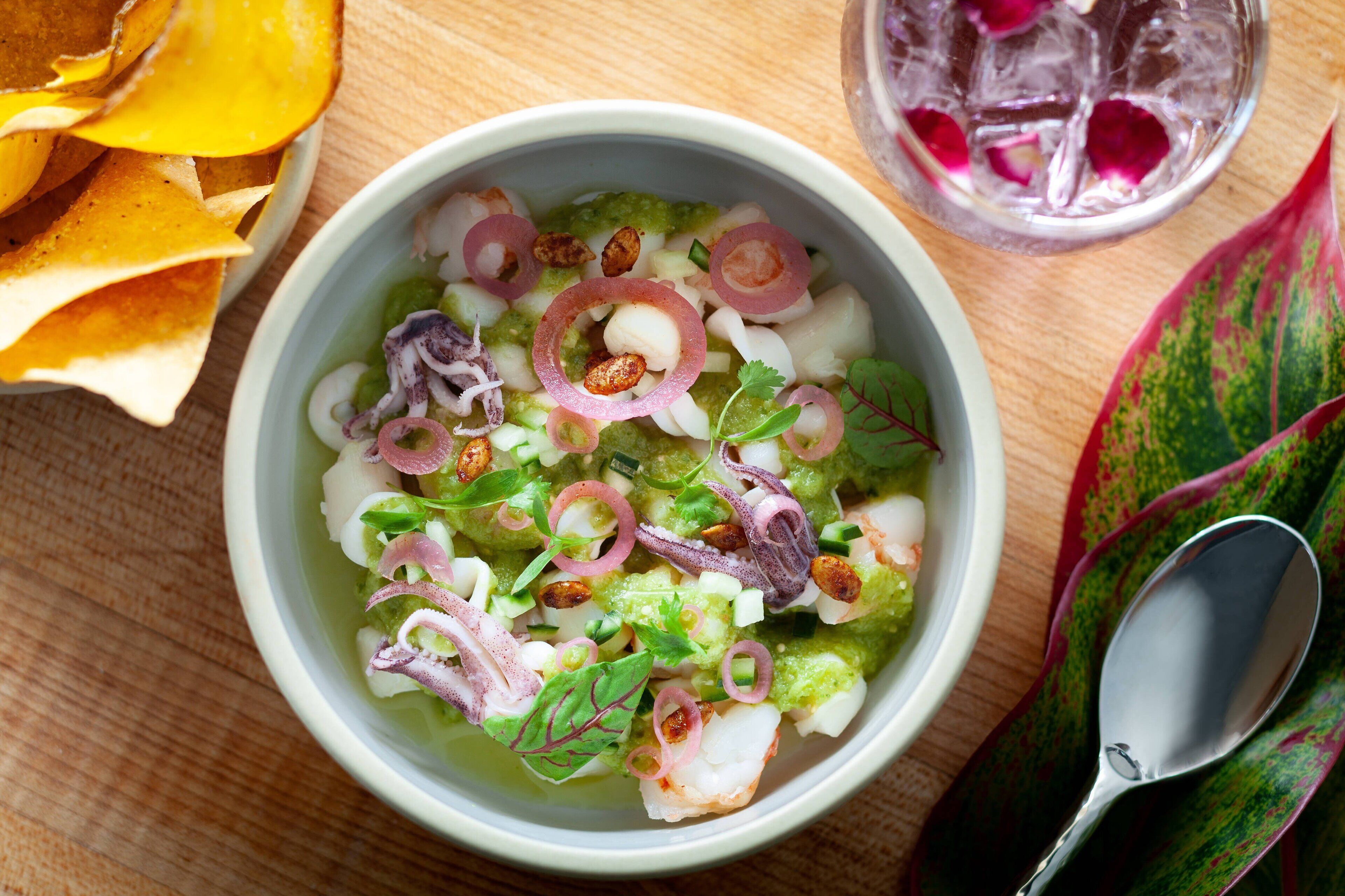A bowl of seafood salad with chips and a glass of iced drink on a wooden table.