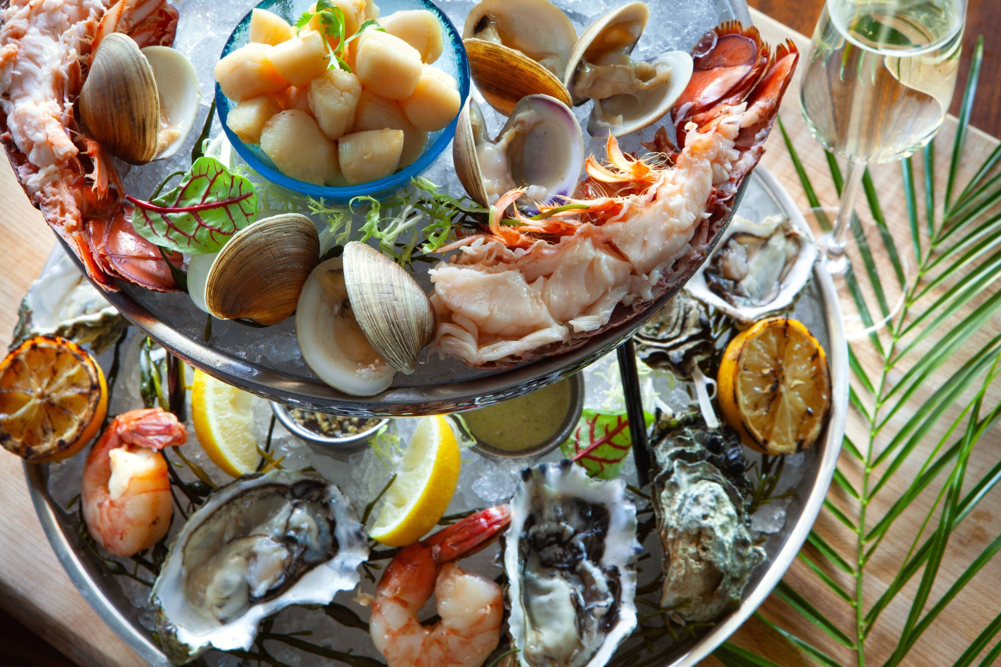 Una bandeja de mariscos con almejas, camarones y ostras sobre hielo, adornada con rodajas de limón y hierbas.