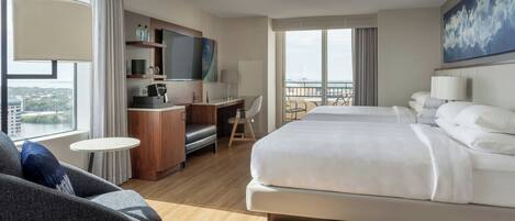 Una habitación de hotel moderna con una cama grande, un escritorio, un televisor y un balcón con vistas a la ciudad.