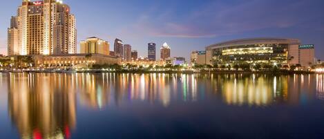 A city skyline with high-rise buildings and a large stadium by a calm body of water.