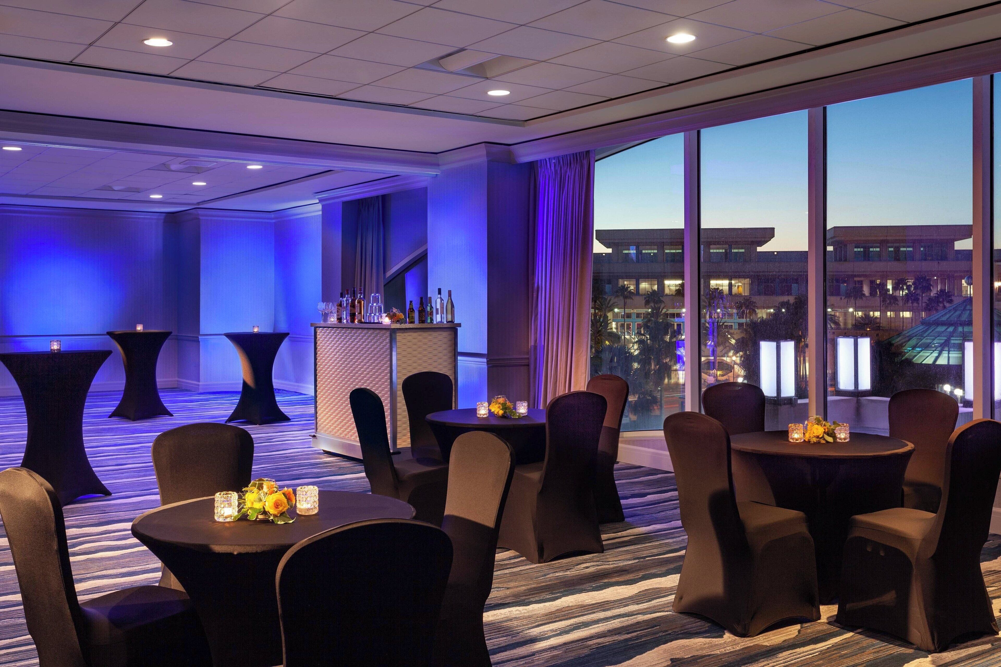 A hotel room with a large window, a bar area, and multiple tables and chairs.