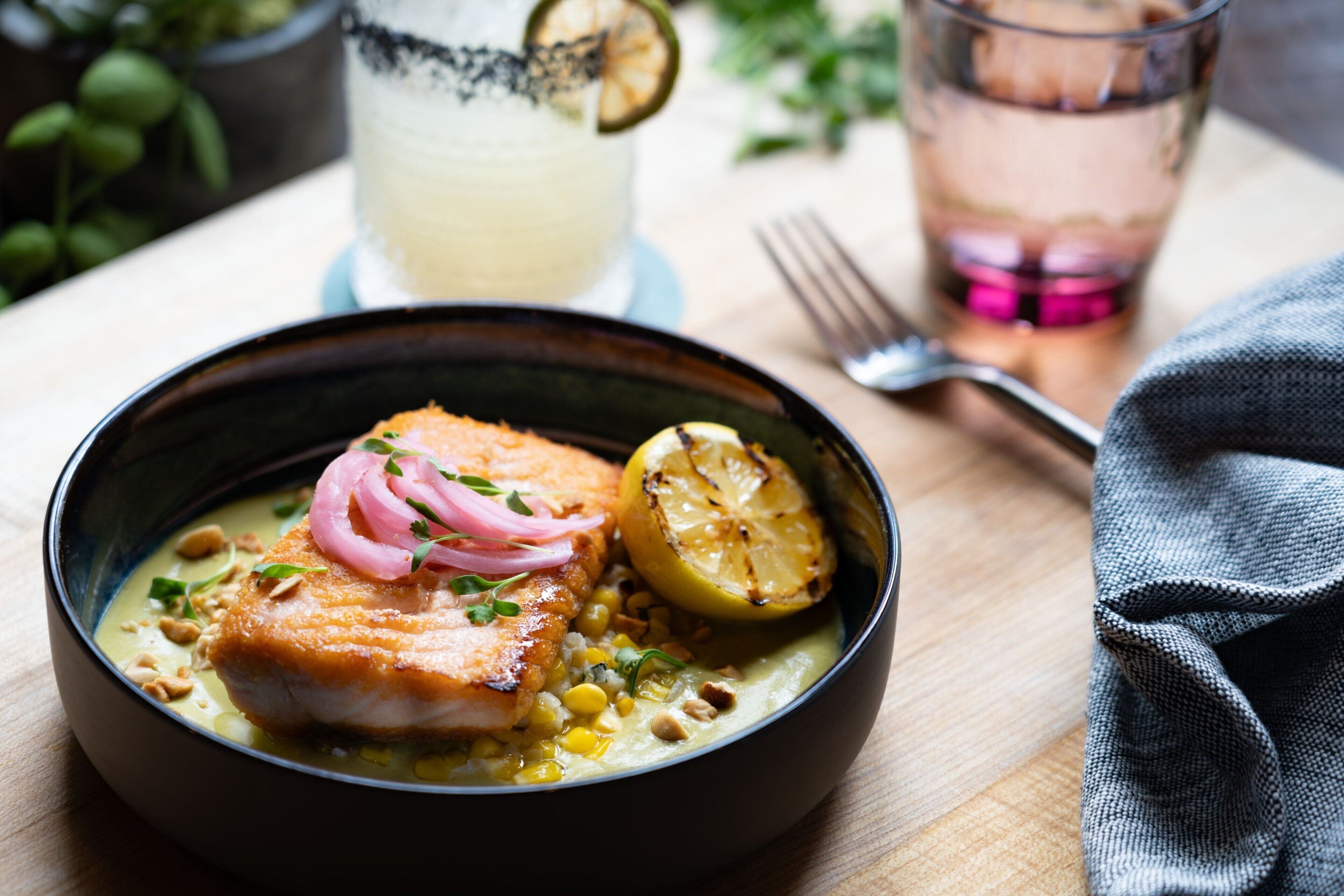 A bowl of food with a piece of fish, lemon, and onions.