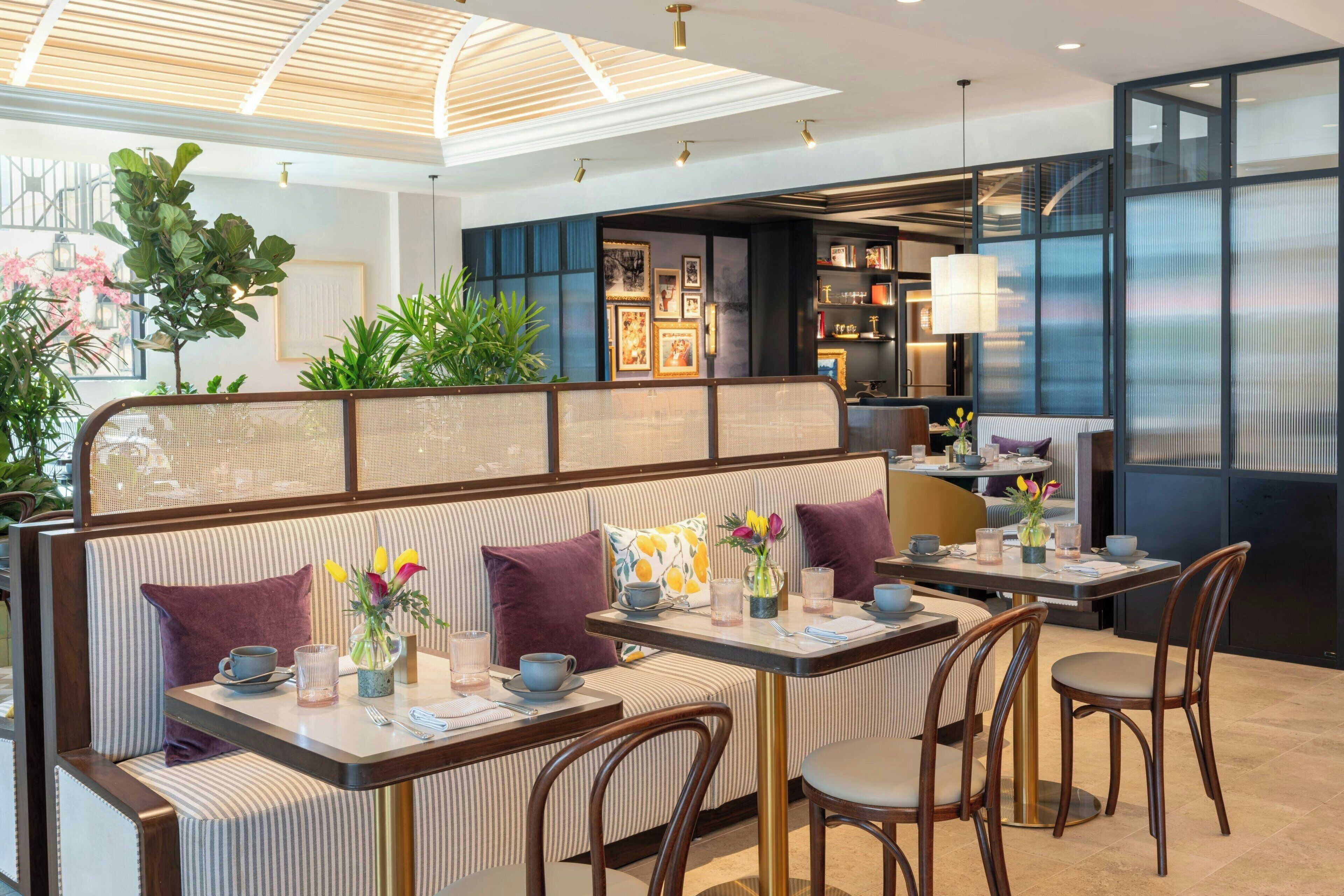 A modern dining area with striped booths, tables, and chairs. There are plants and framed pictures on the walls.