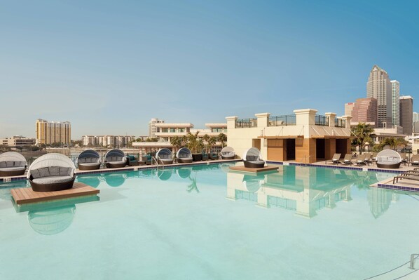 A rooftop pool with lounge chairs, a city skyline in the background, and a clear sky.
