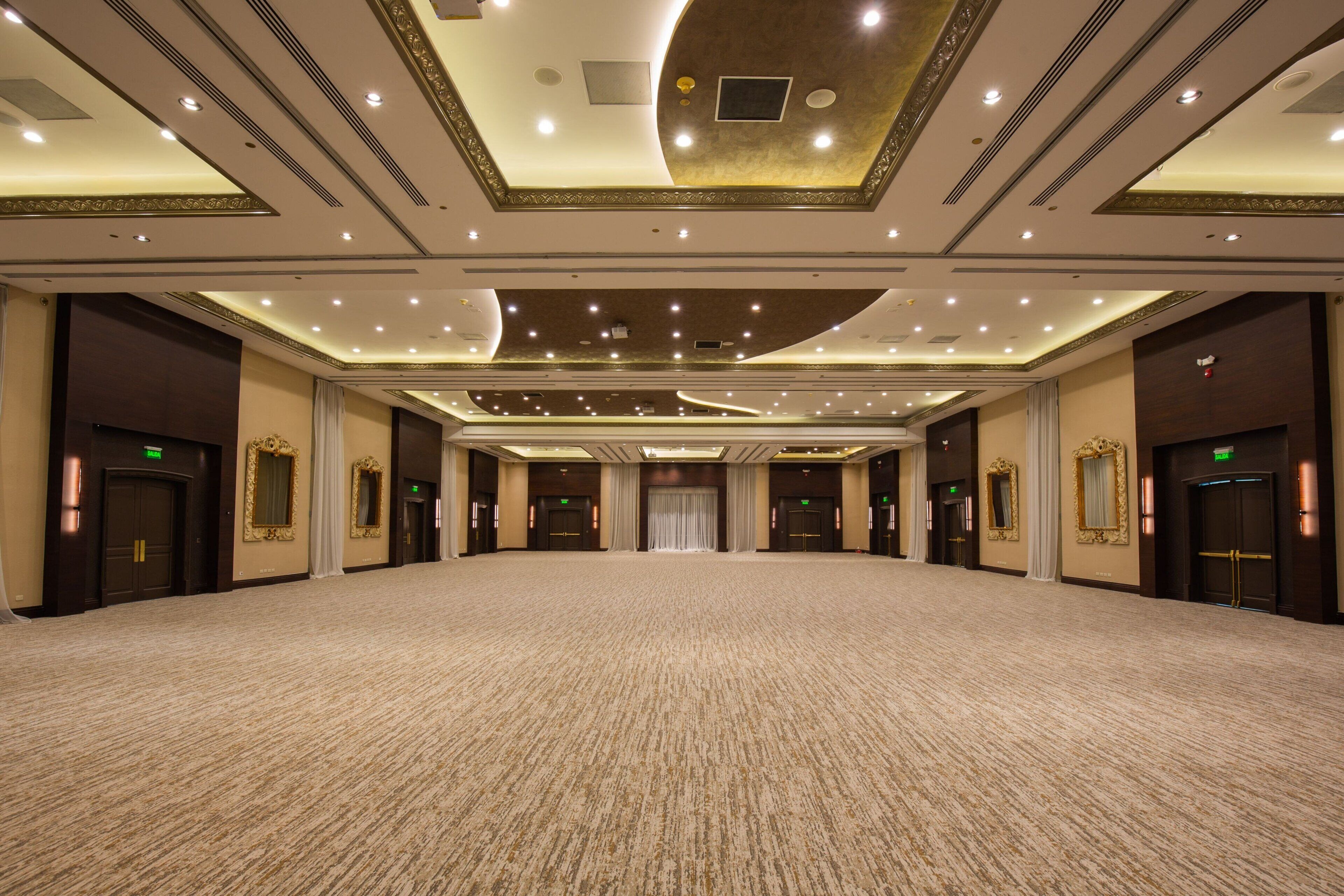 A large, carpeted room with multiple doors, recessed lighting, and decorative ceiling elements.