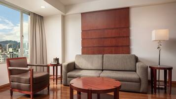 A modern hotel room with a sofa, armchair, and round wooden coffee table.