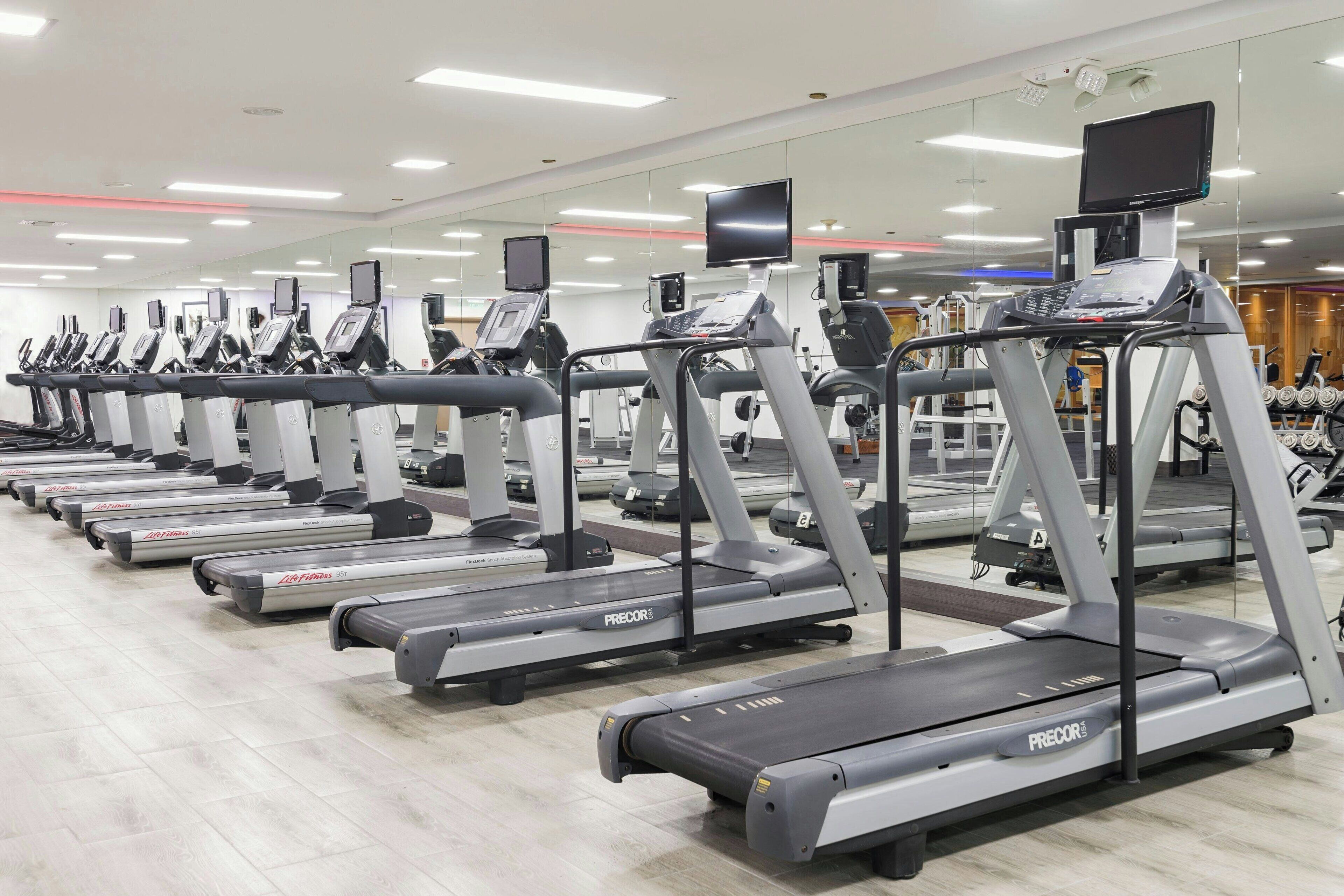 A row of treadmills in a gym with mirrored walls and ceiling lights.