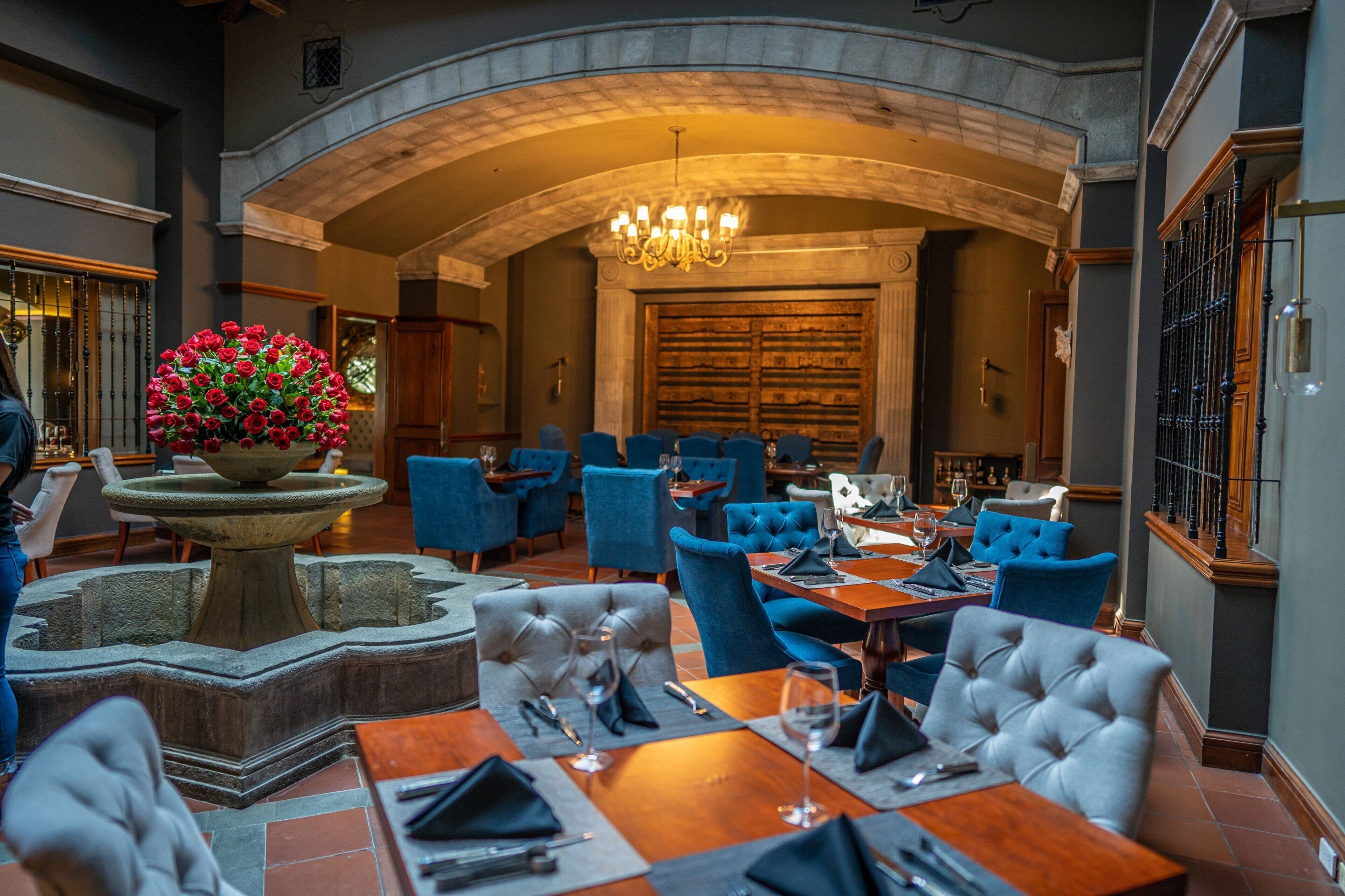 A restaurant with a stone fountain centerpiece, blue upholstered chairs, and a chandelier.