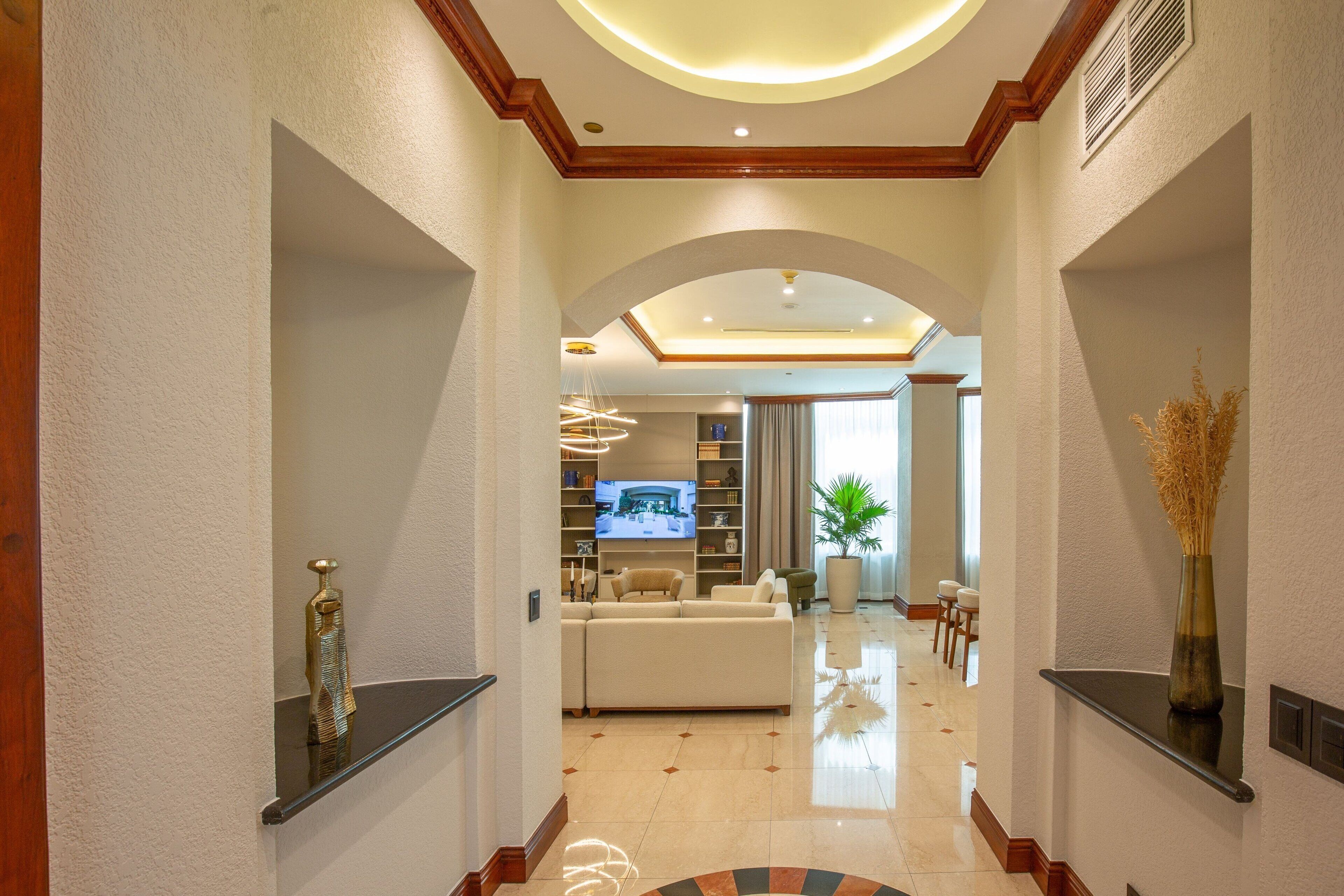 A modern hotel lobby with a central seating area, a flat-screen TV, and a large potted plant.