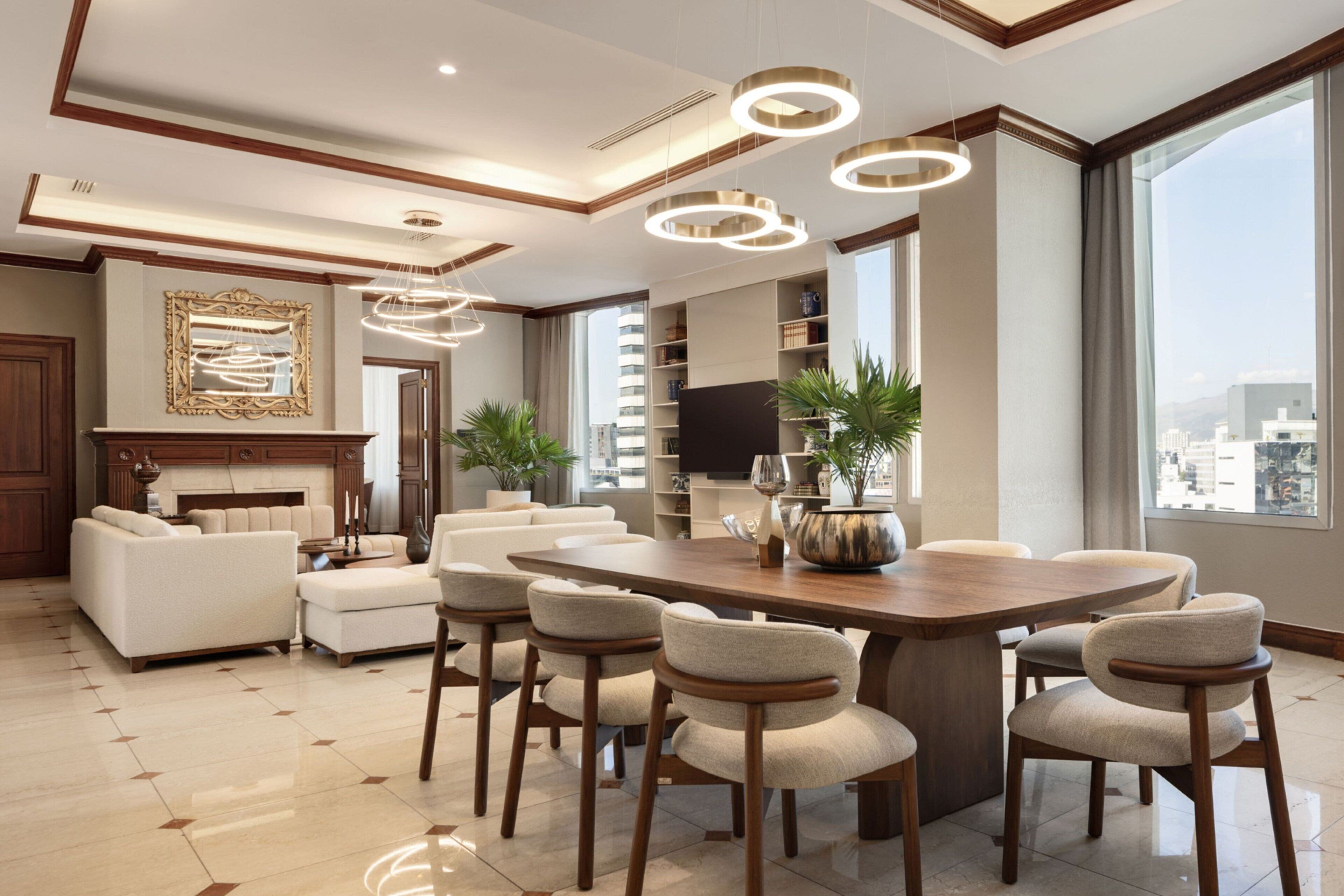 Uma sala de estar espaçosa com uma grande mesa de jantar de madeira rodeada por cadeiras, uma lareira e um amplo janelão com vista para a cidade.