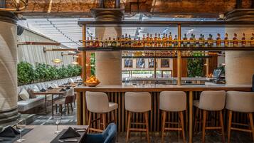 Una zona de bar con taburetes de madera, una variedad de botellas y un área de asientos con bancos y mesas acolchados.