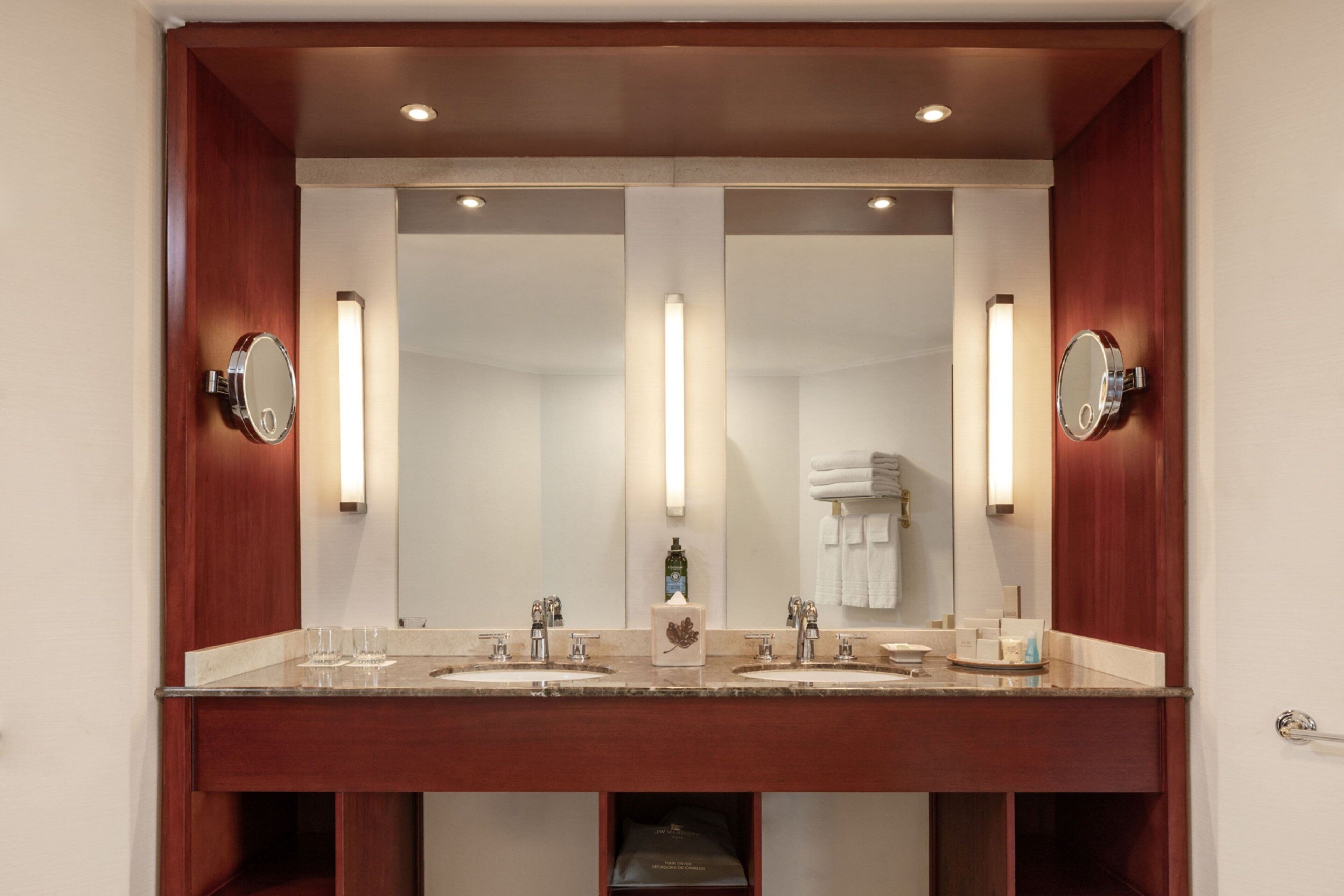 A hotel bathroom with a double sink vanity, two wall-mounted mirrors, and a towel rack.
