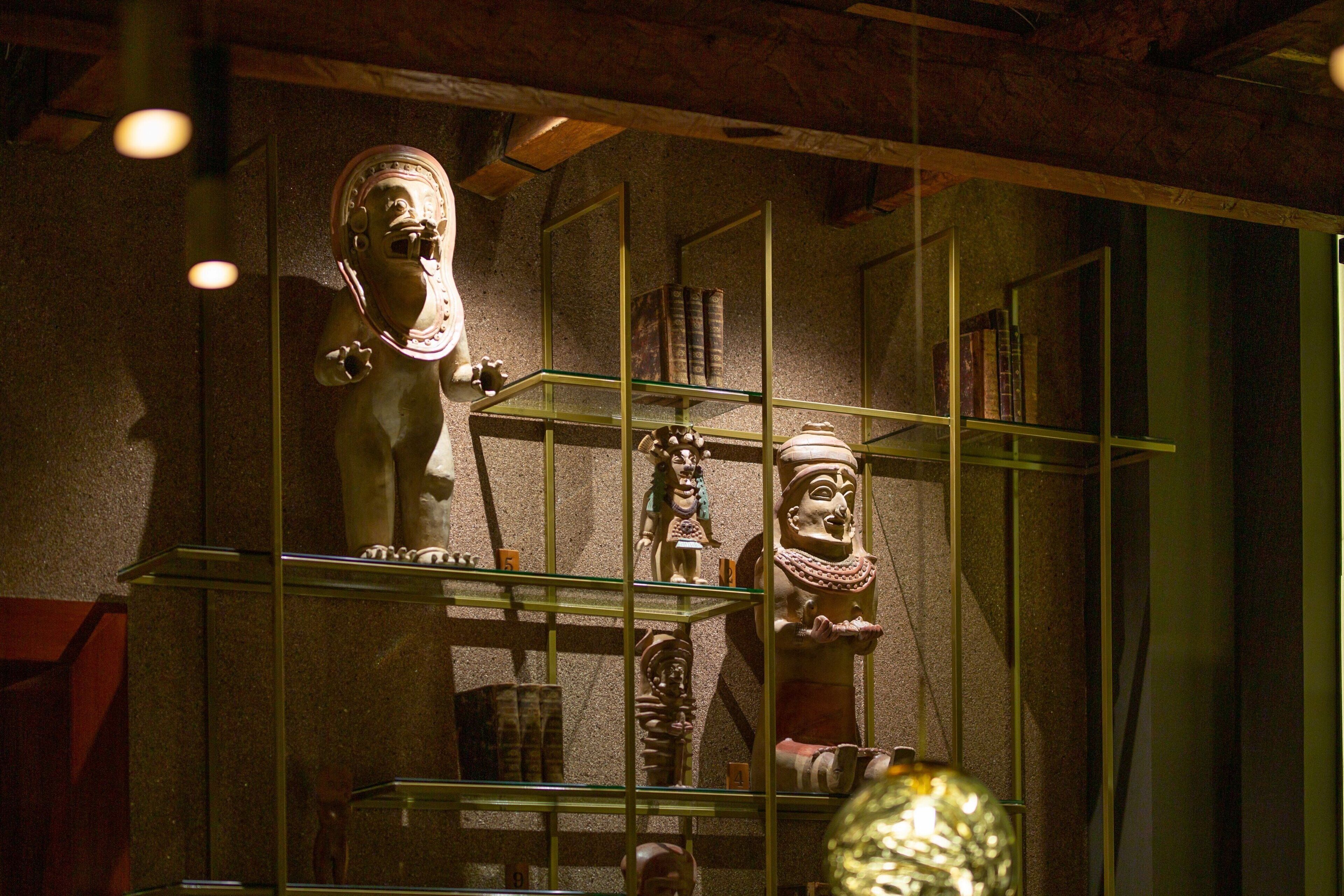 En museumsudstilling med glashylder, der viser forskellige oldtidsartefakter og skulpturer.