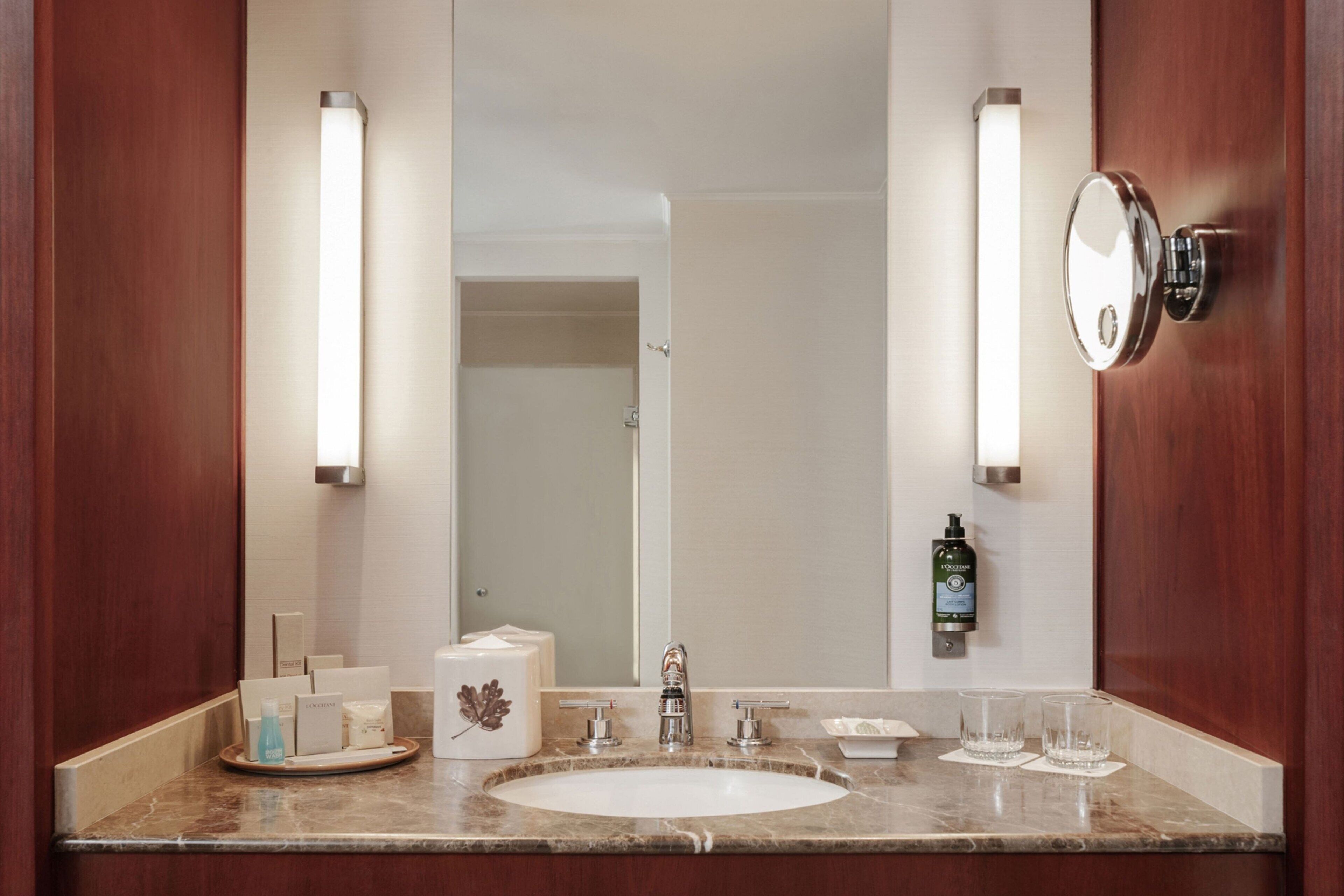 A hotel bathroom with a marble sink, two wall-mounted lights, a mirror, and toiletries on the counter.
