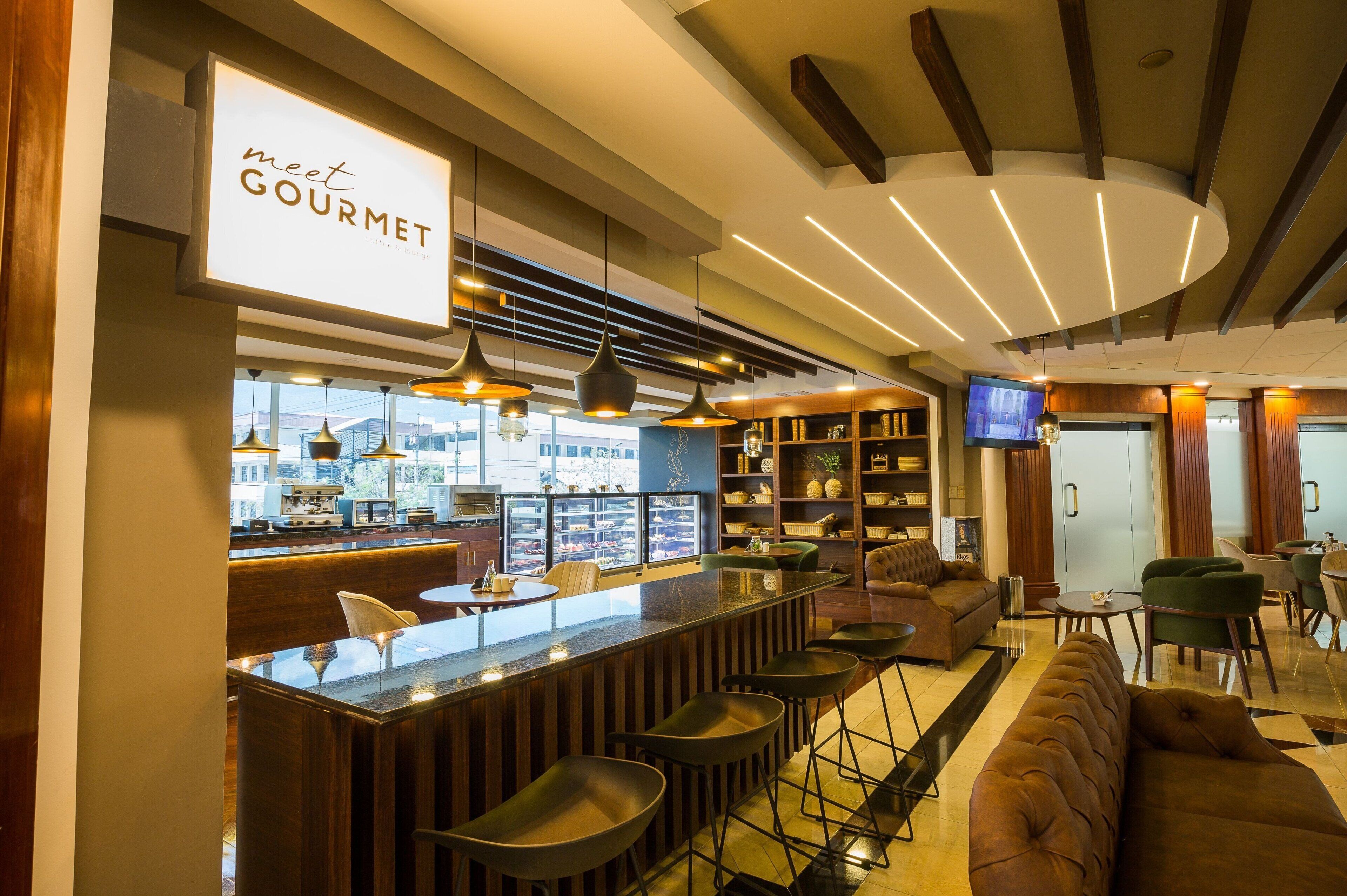 A modern bar area with a 'meet GOURMET' sign, bar stools, a sofa, and a television.