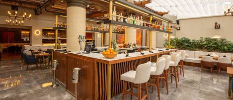 A bar area with a wooden bar counter, multiple seating options, and a variety of bottles and glasses on shelves.