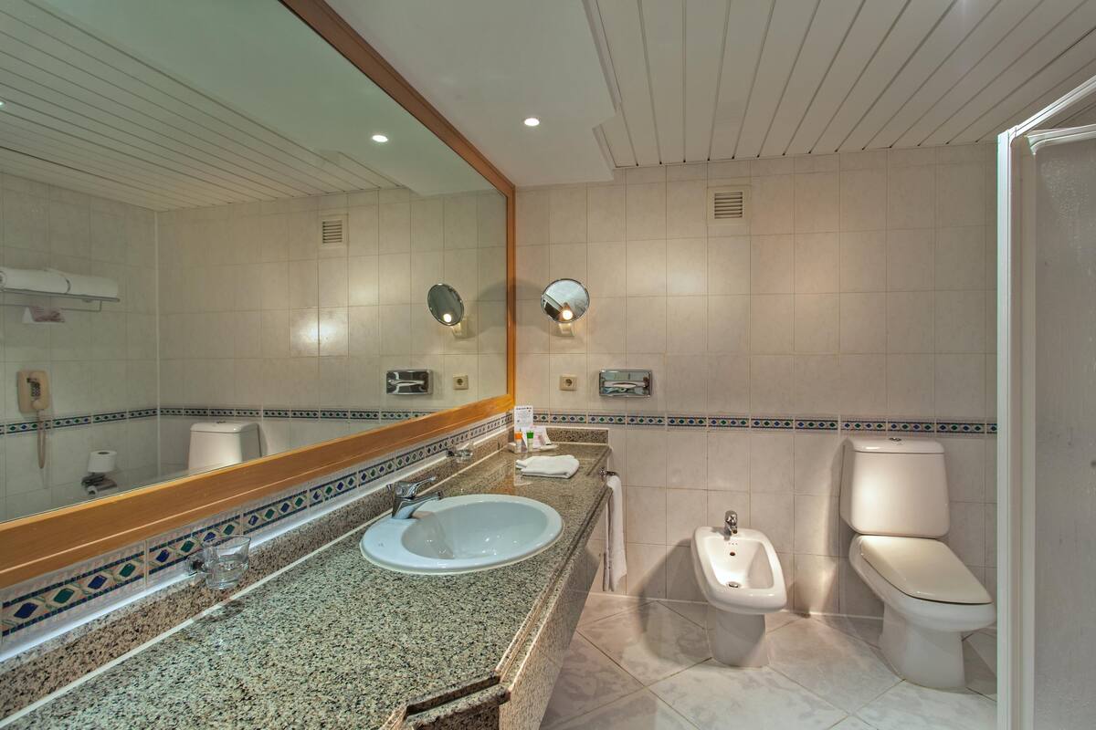 A bathroom with a sink, mirror, bidet, toilet, and tiled walls.