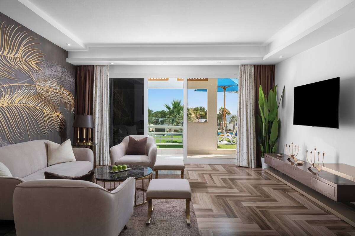 A modern living room with a sofa, armchair, and ottoman, a coffee table, a TV, and a large plant.
