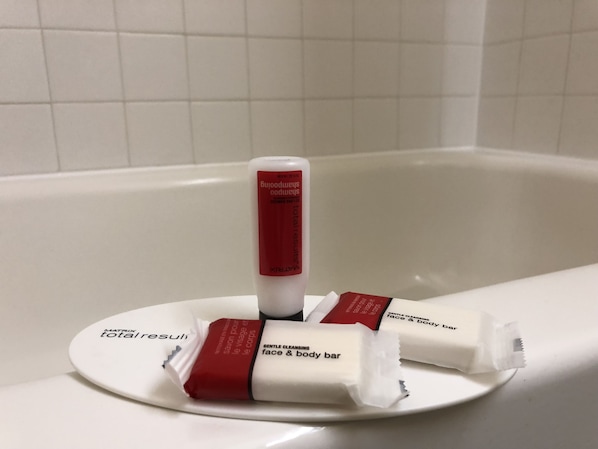 A bathroom with a white bathtub and a white sink. There are three white and red bars of soap on the sink.