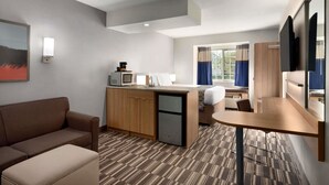 A compact hotel room with a kitchenette, a sofa, a small table, and a bed. - Microtel Inn & Suites by Wyndham Baton Rouge (Baton Rouge)