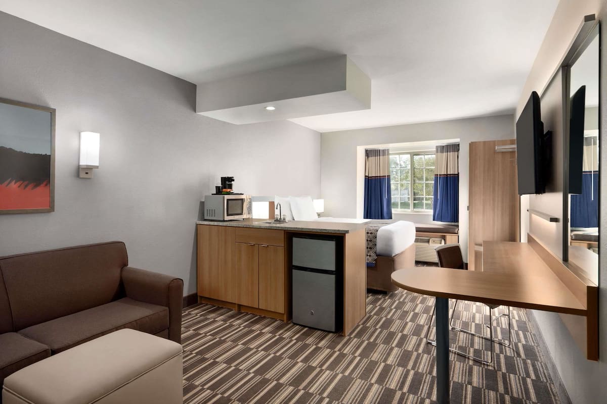 Una habitación de hotel compacta con kitchenette, un sofá, una pequeña mesa y una cama.
