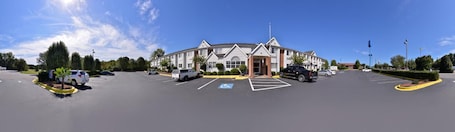 A large, modern building with a symmetrical facade, multiple parking spaces, and a clear blue sky.