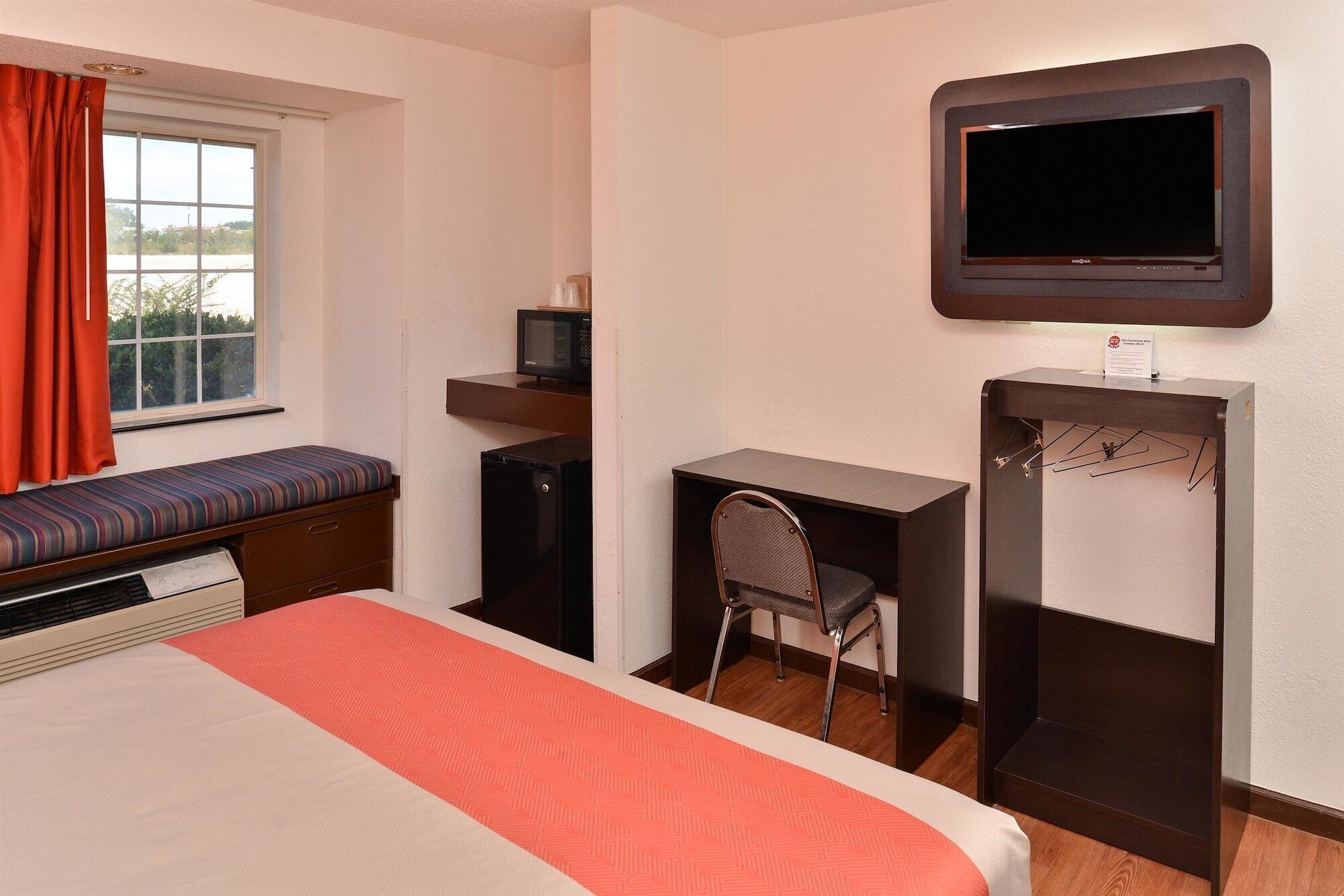 Habitación de hotel con cama, escritorio, silla, televisión y un estante pequeño con un microondas.