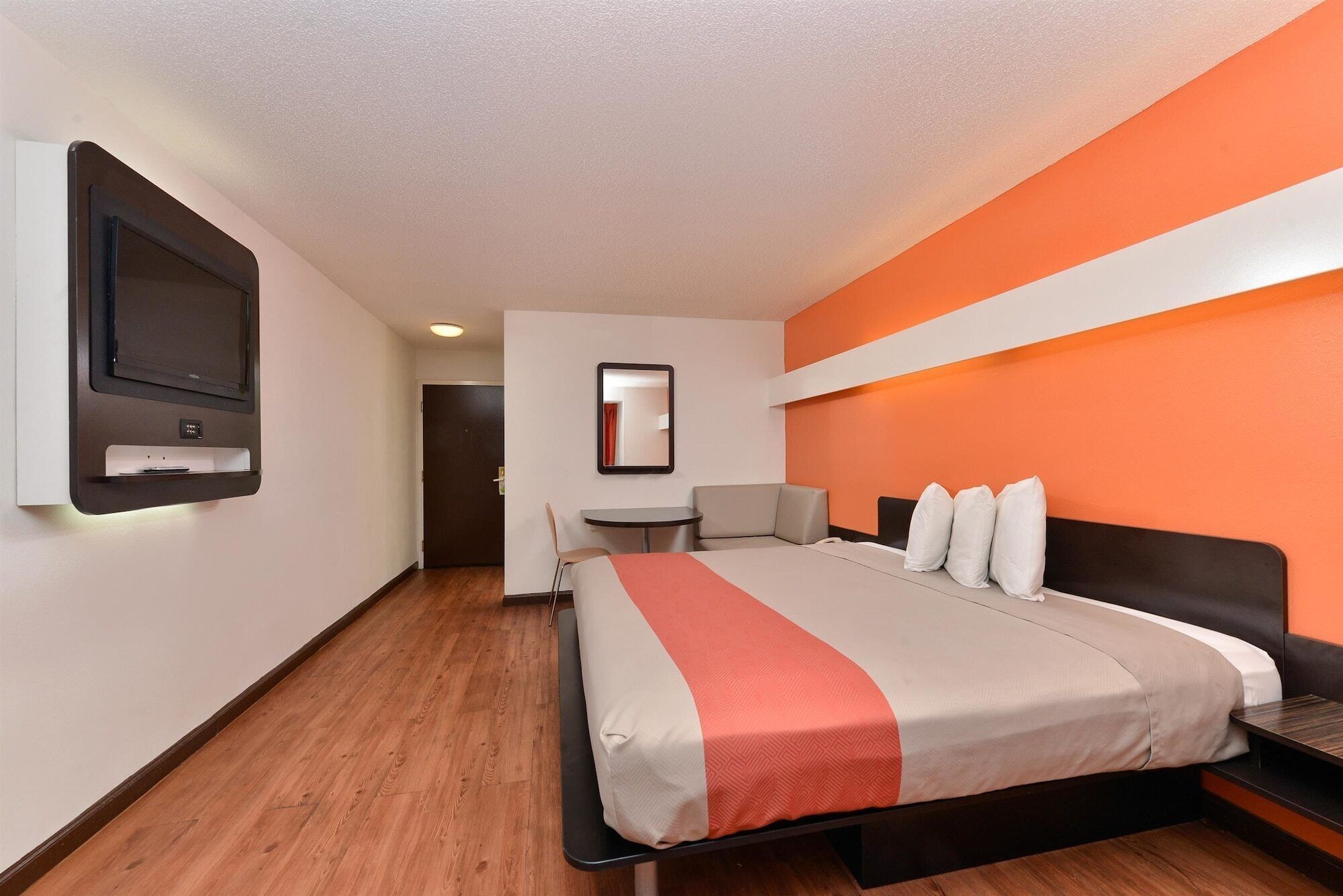 A hotel room with a bed, a desk, a chair, a TV, and a mirror.