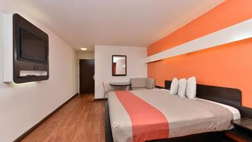 A hotel room with a bed, a desk, a chair, a TV, and a mirror.
