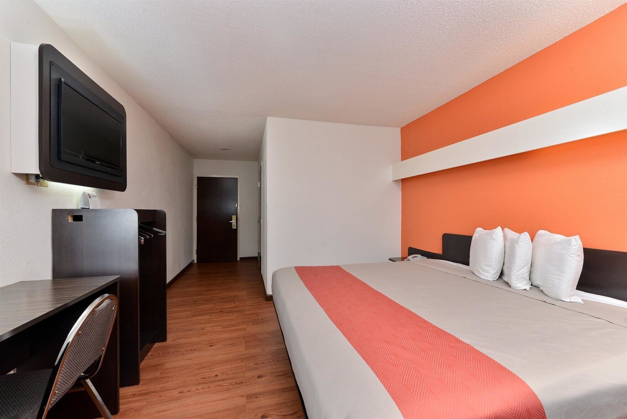 Una habitación de hotel con una cama, un escritorio, una silla, un televisor y una puerta.