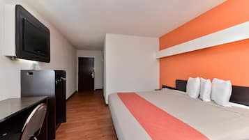 Una habitación de hotel con una cama, un escritorio, una silla, un televisor y una puerta.