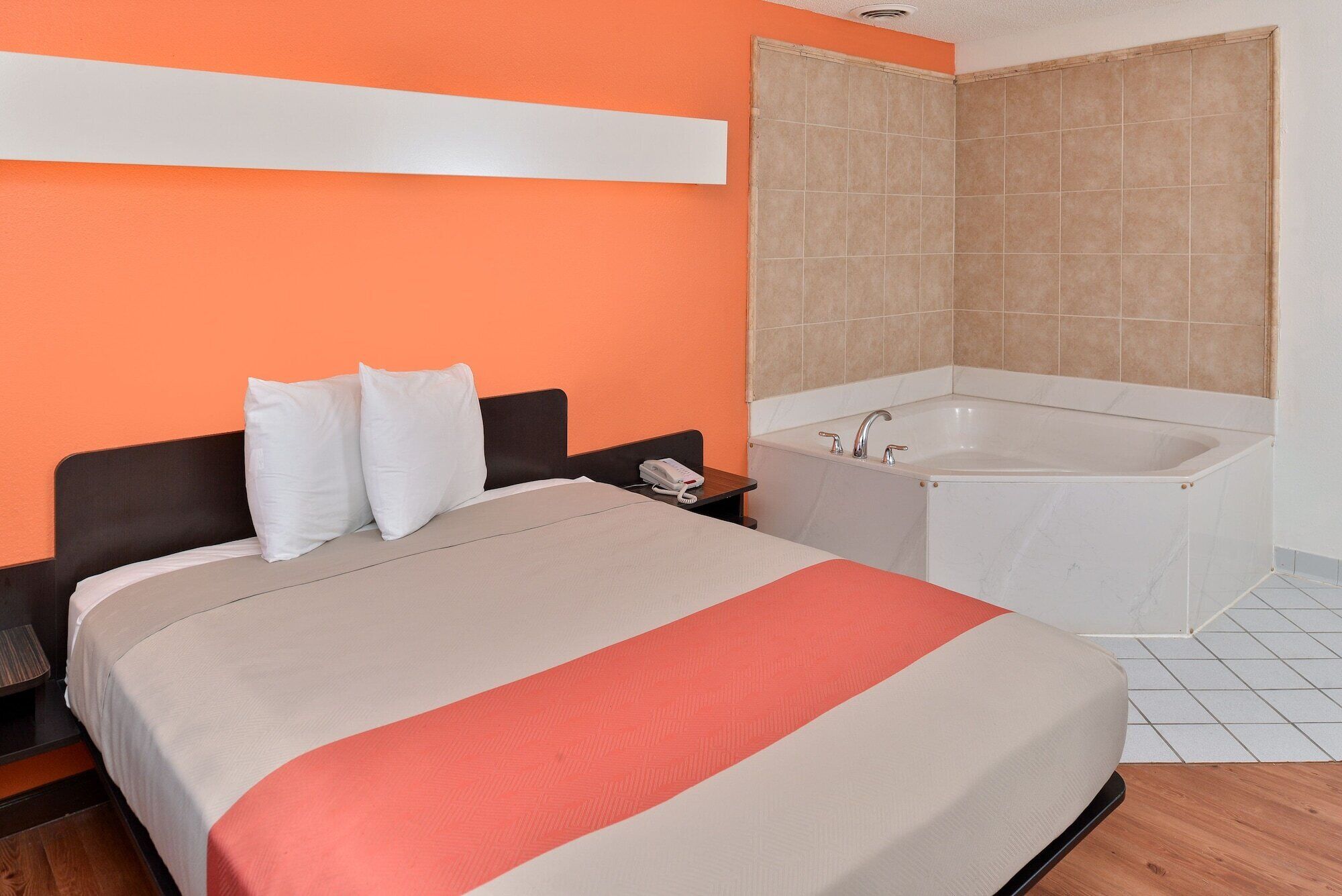 Habitación de hotel con cama, mesita de noche, teléfono y baño con bañera y paredes de azulejos.