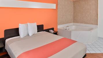Habitación de hotel con cama, mesita de noche, teléfono y baño con bañera y paredes de azulejos.