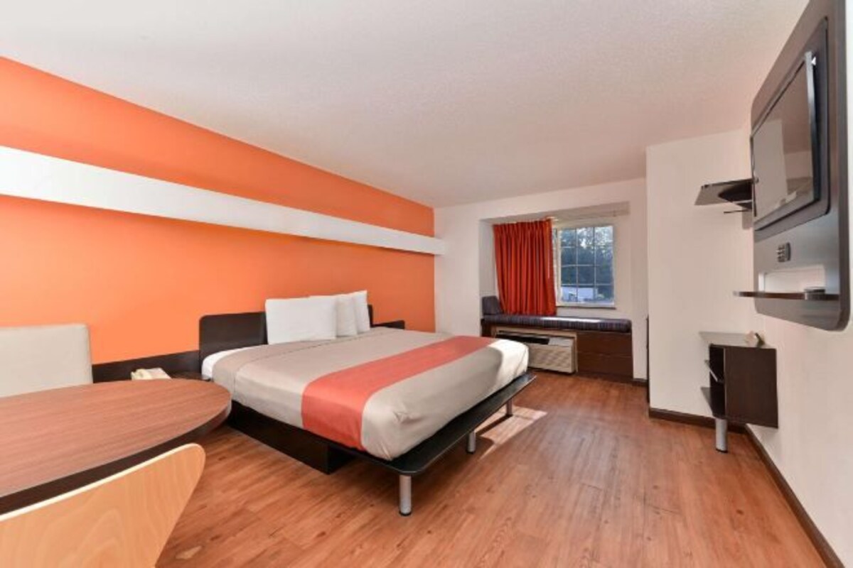 Ett hotellrum med en säng, ett skrivbord, en stol, en tv och ett fönster med gardiner.