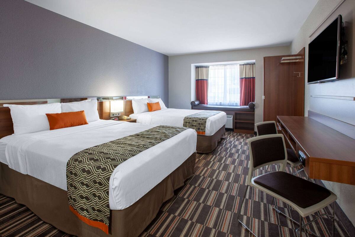 Una habitación de hotel con dos camas, un escritorio, un televisor y una ventana con cortinas.