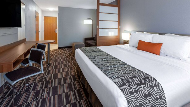 A hotel room with a bed, a desk, a chair, a TV, and a lamp. - Microtel Inn & Suites by Wyndham Sunbury/Columbus North (Sunbury)