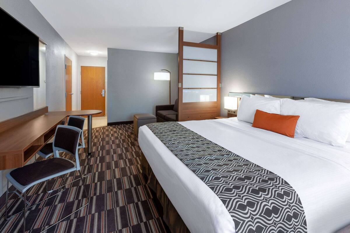 Una habitación de hotel con cama, escritorio, silla, televisor y lámpara.