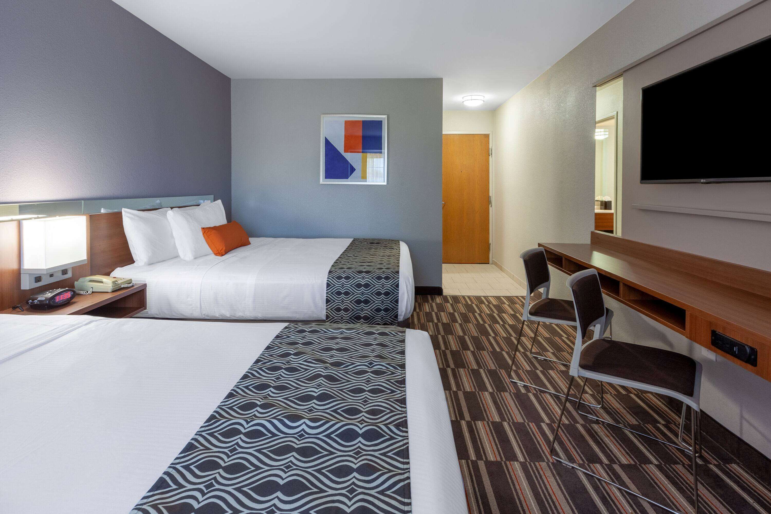 A hotel room with two beds, a desk, a chair, a flat-screen TV, and a painting on the wall.