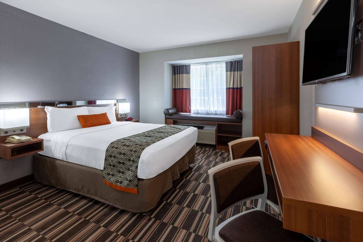 Habitación de hotel con cama, escritorio, silla, televisor y ventana con cortinas.