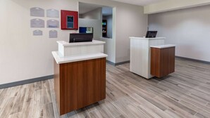 A reception area with two wooden reception desks, a digital display, and a set of informational plaques on the wall. - Microtel Inn & Suites by Wyndham Sunbury/Columbus North (Sunbury)