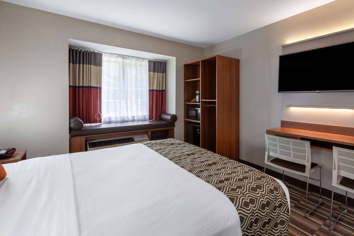 Una habitación de hotel con una cama grande, un escritorio con silla, un televisor y un armario.