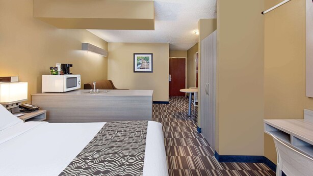 Habitación de hotel con cama, escritorio con microondas, una silla, una mesita y un cuadro en la pared.