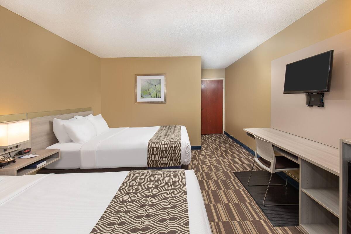 A hotel room with two beds, a desk, a chair, a television, and a door.