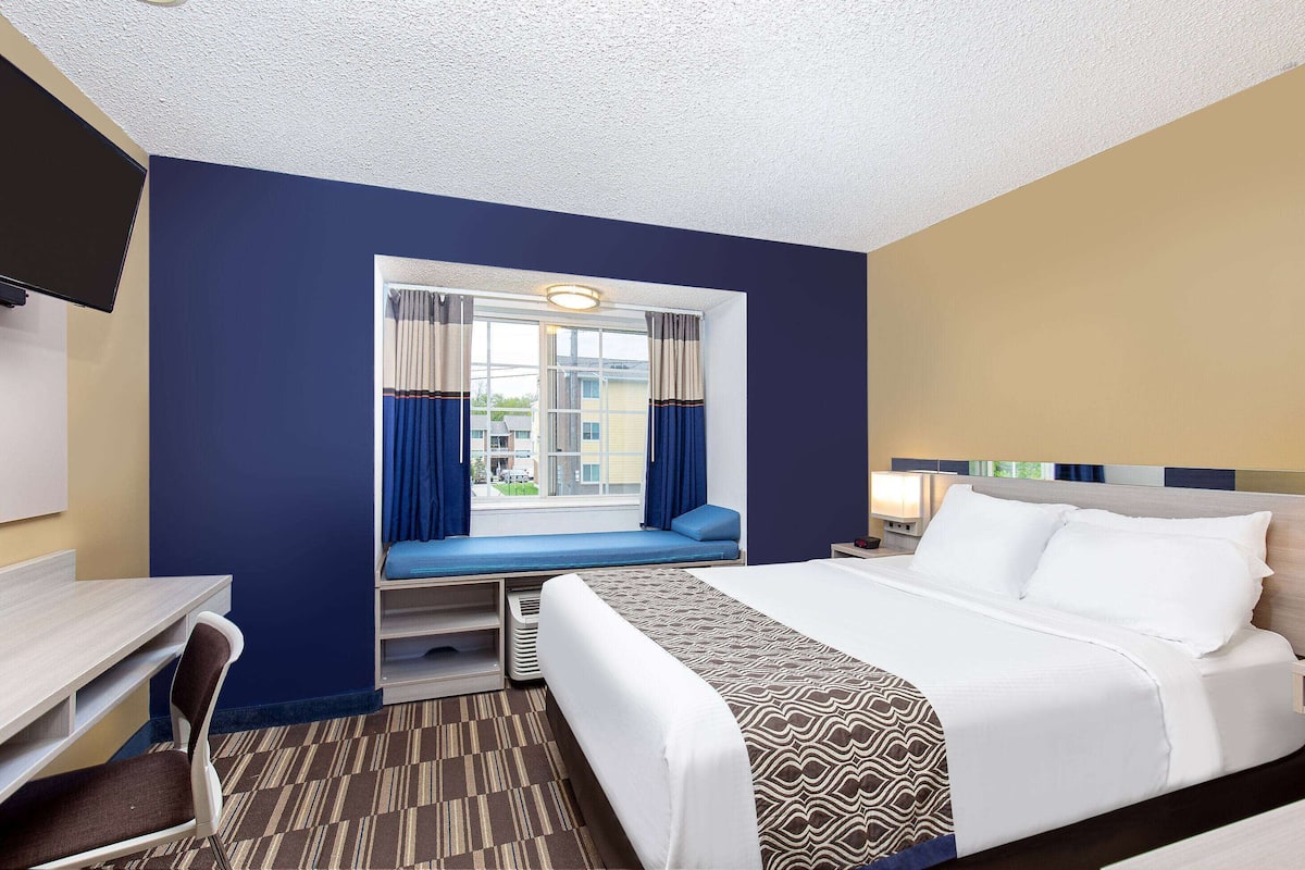 A hotel room with a bed, a desk, a chair, a window with curtains, and a television on the wall.